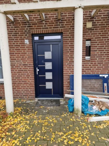 Blauwe voordeur met vier glazen panelen, omringd door herfstbladeren.